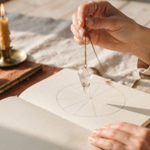 Manos con un péndulo sobre una tabla radiónica, portada del curso Nudo Cero